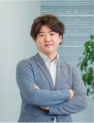グレーのジャケットを着た人物が腕を組んで立つ