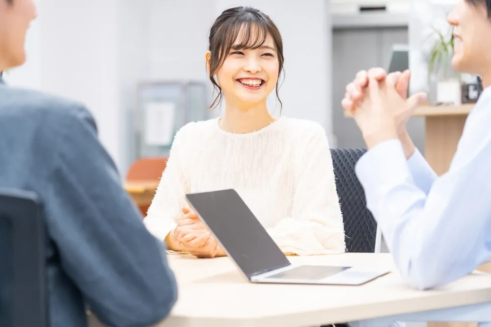 ノートパソコンを前に笑顔で話す打ち合わせ中の女性