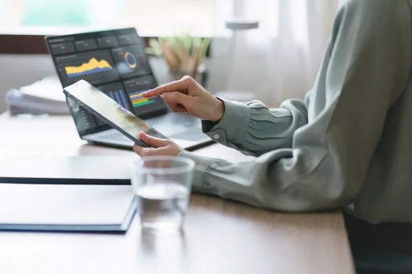 営業データを分析するノートパソコンとタブレットを操作する女性