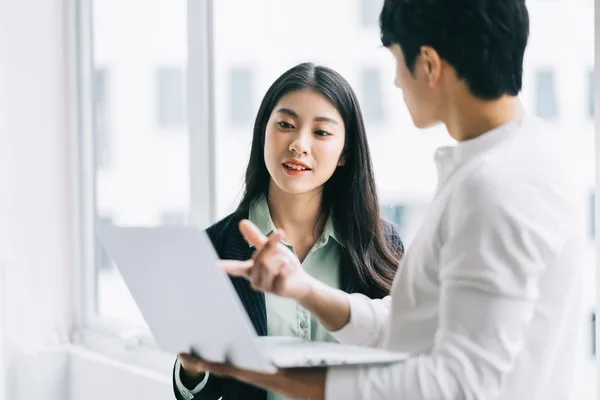 ノートパソコンを見ながら営業戦略について打ち合わせする男女