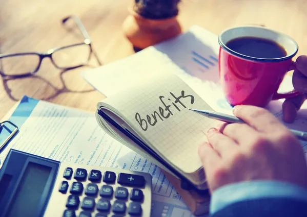 ノートに「benefits」と書き込む手、デスク上の電卓とコーヒーカップ
