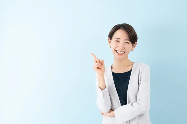 白いカーディガンを着た女性が笑顔で右上を指差している