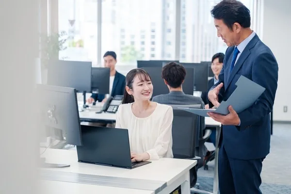 ノートパソコンを操作する女性社員と書類を持つ男性上司