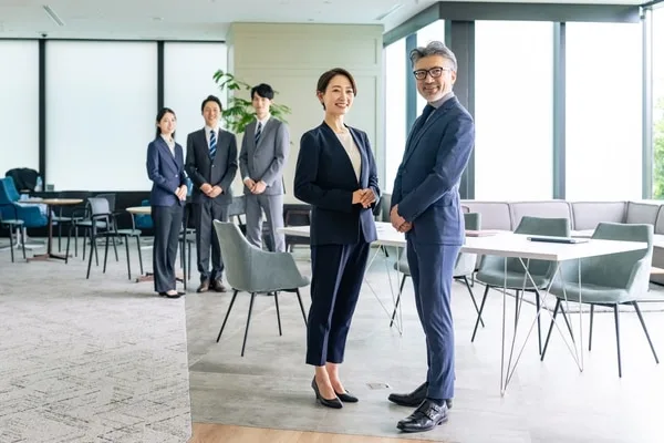 オフィスに立つスーツ姿の男女と後方の同僚