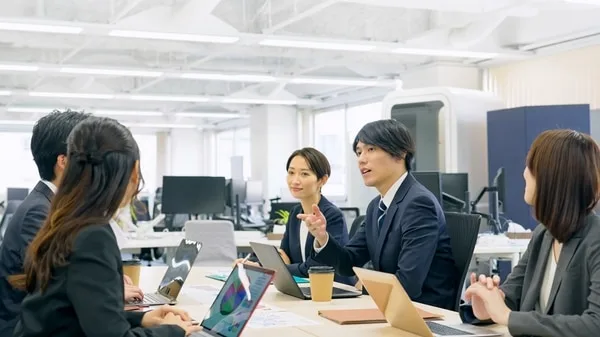 オフィスの会議テーブルを囲み話し合う社員