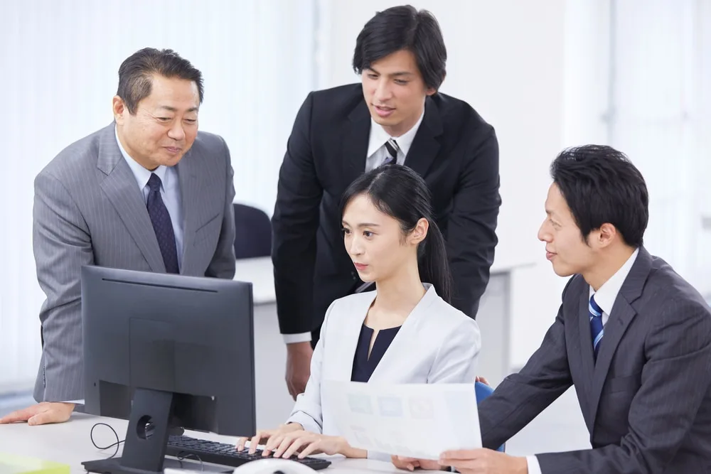 営業チームがパソコン画面を確認しながら会議をしている