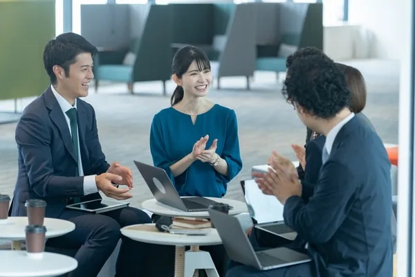 ラウンジでノートパソコンを囲み話し合う社員