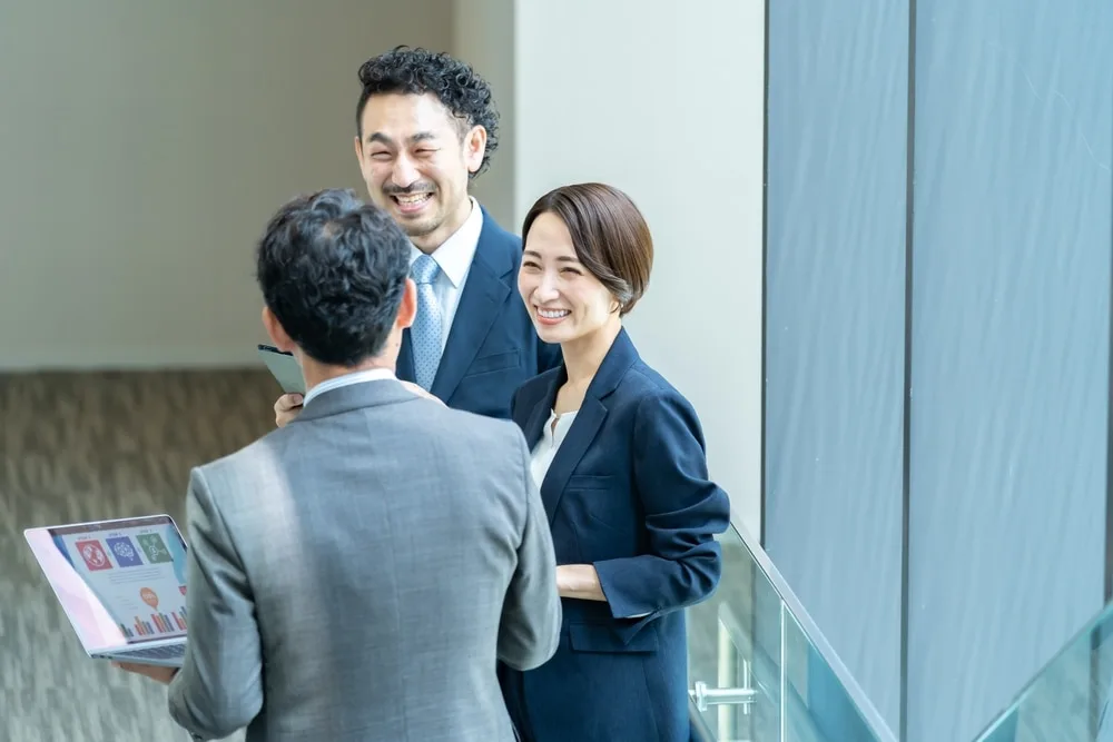 三人のビジネスパーソンがオフィスで笑顔で会話している様子