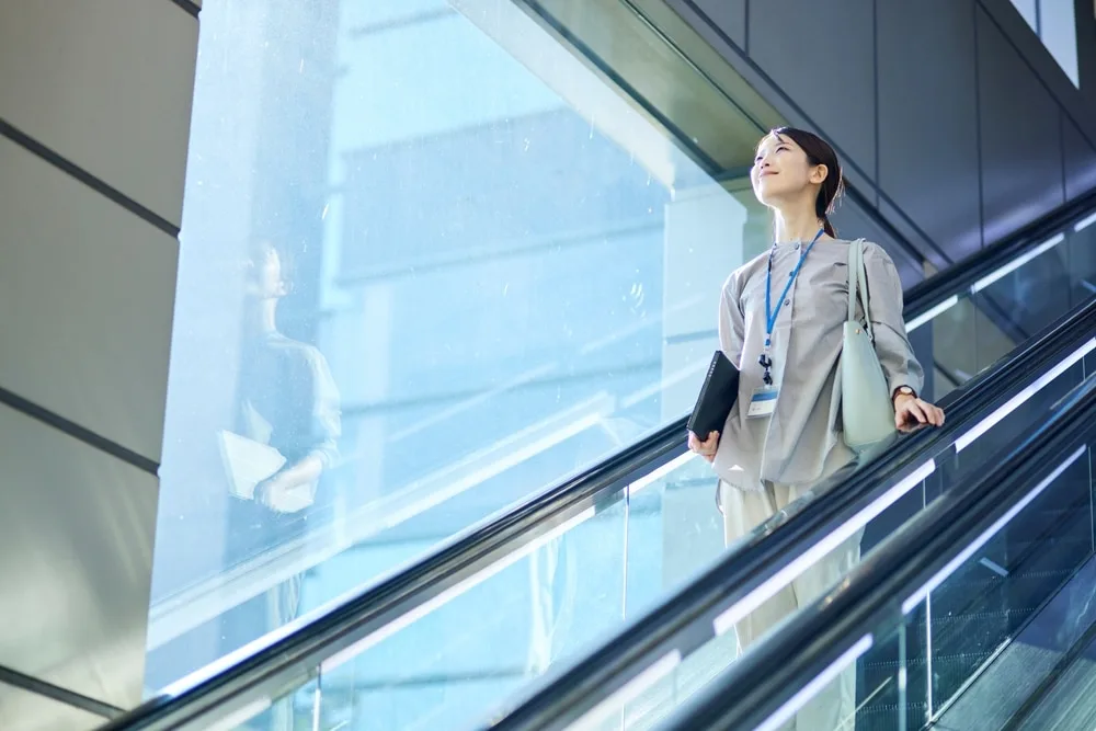 エスカレーターで上昇する女性営業担当者