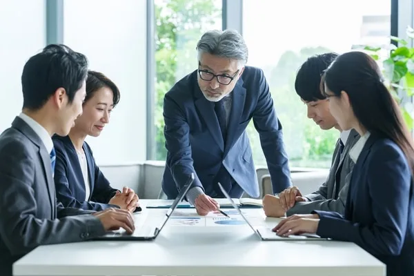 営業チームがテーブルを囲んで資料を確認しながら打ち合わせしている光景