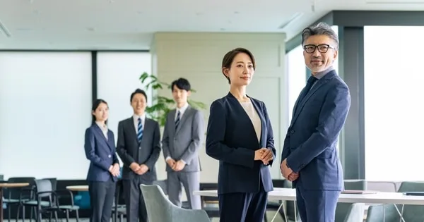 オフィスに並んで立つ男女と背後の社員3人