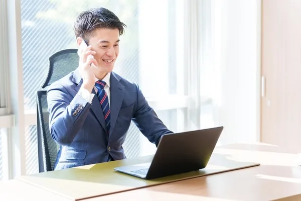 スーツ姿の男性がノートパソコンを見ながら電話で会話