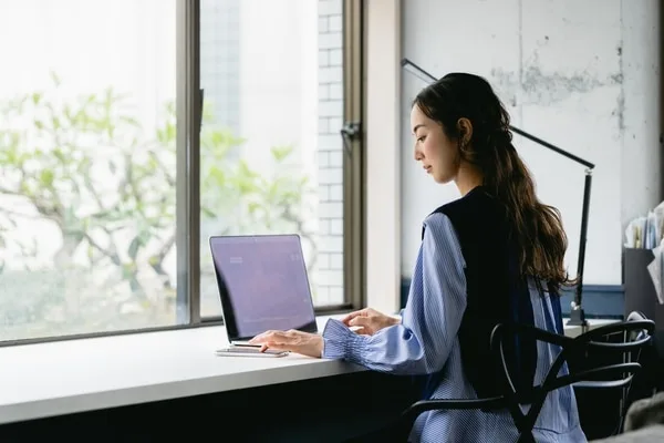 窓際でノートパソコンを操作する女性営業職