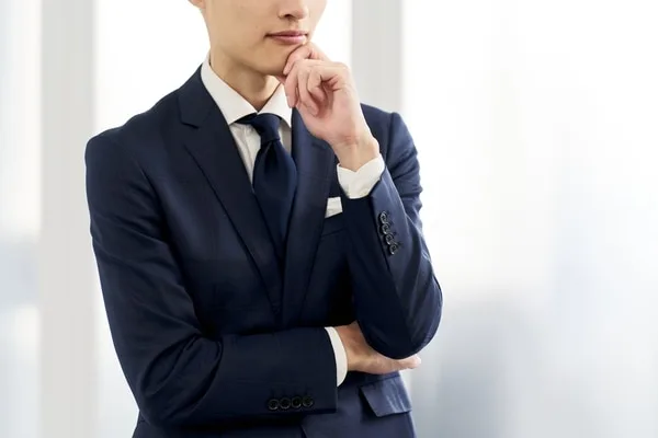 ビジネススーツを着た男性が考えるポーズで立っている。