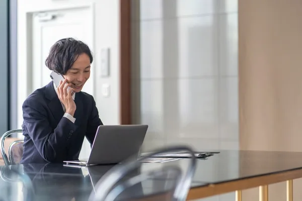 電話をしながらノートパソコンで営業業務を進める女性営業職