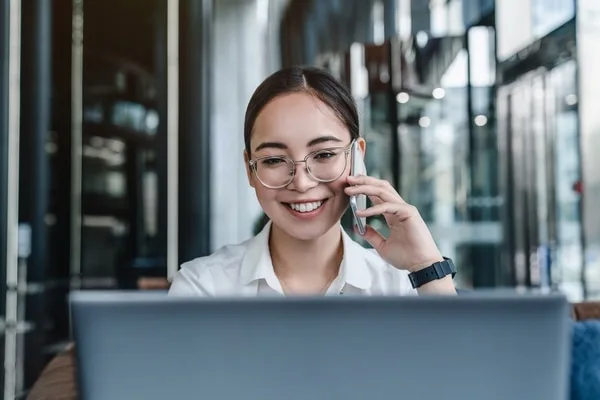 眼鏡をかけた女性がノートパソコンを前にスマートフォンで通話