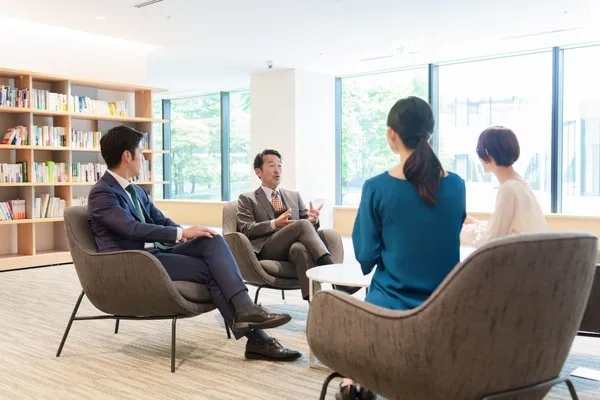 オフィスラウンジでビジネスパーソン4人が椅子に座り会議する風景