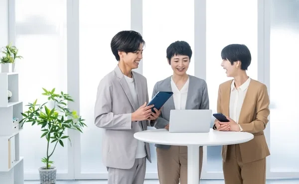 タブレットとノートパソコンを見ながら打ち合わせする営業担当者3人