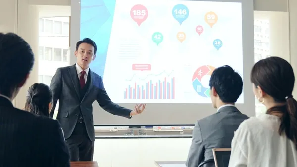 ビジネスマンがプロジェクター画面のグラフを指しながら営業チームに説明