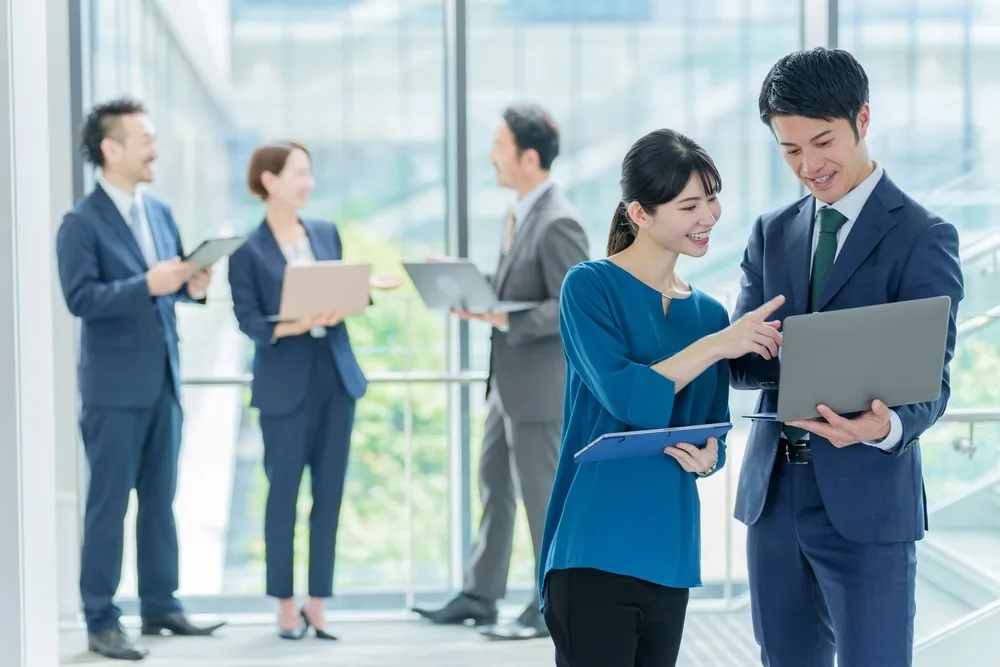 ビジネスパーソンがオフィスでノートパソコンを持ちながら会話