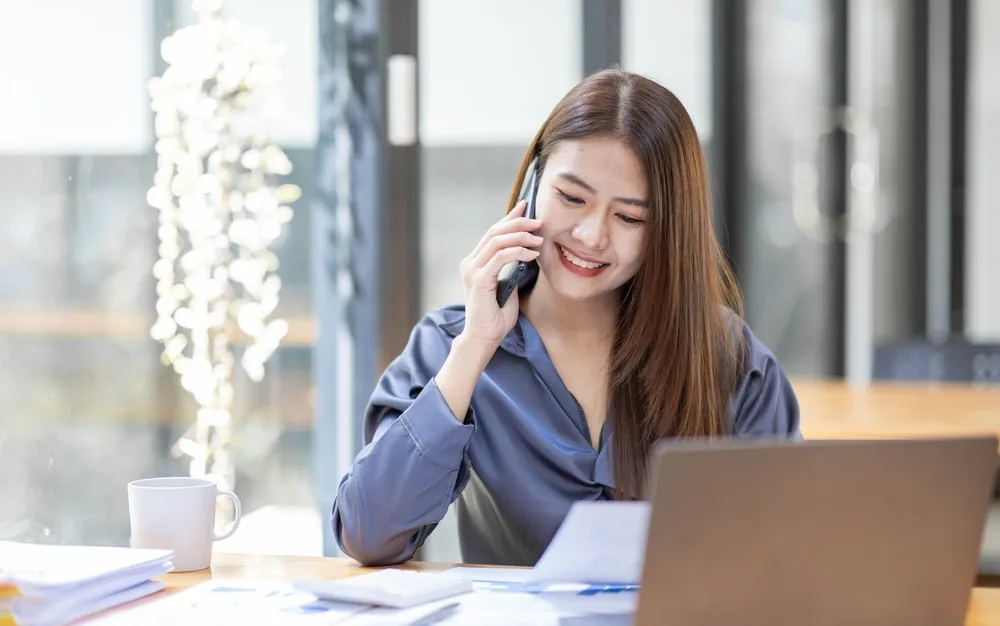 スマートフォンで通話する女性営業担当者がデスク業務をしている
