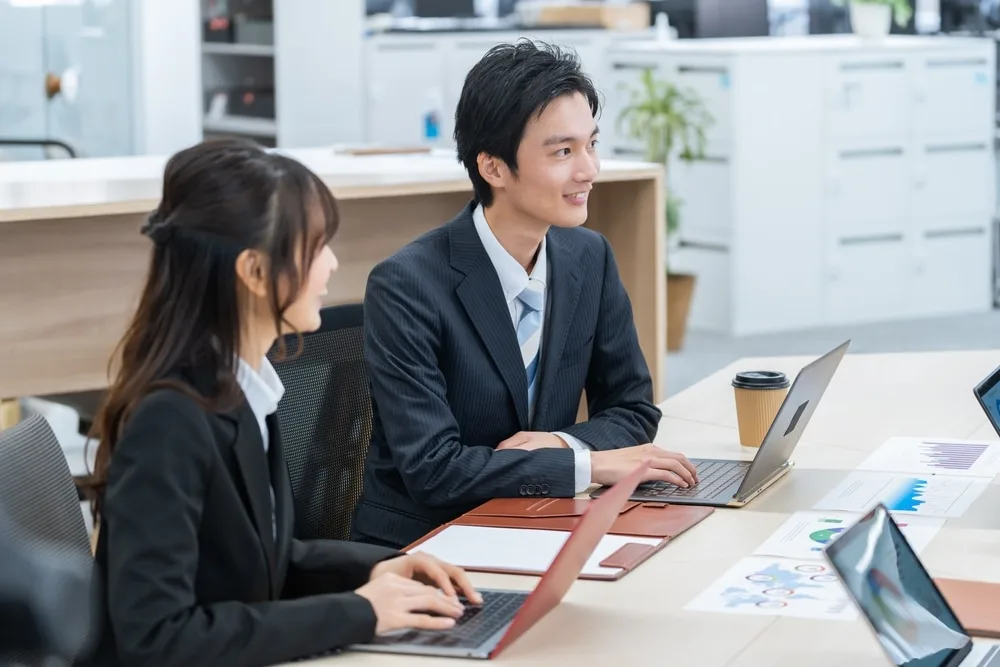 オフィスでノートパソコンを操作しながら打ち合わせする営業スタッフ