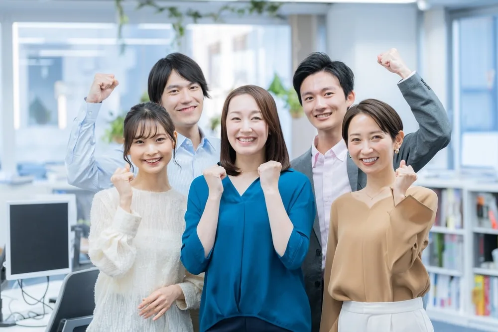 オフィス環境で5人の社員がガッツポーズをして笑顔でカメラを向いている