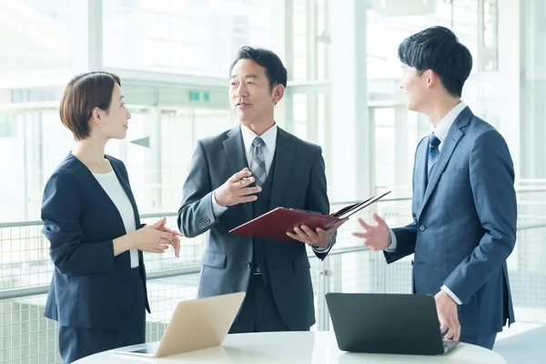 オフィスで3人が資料を囲んで打ち合わせ