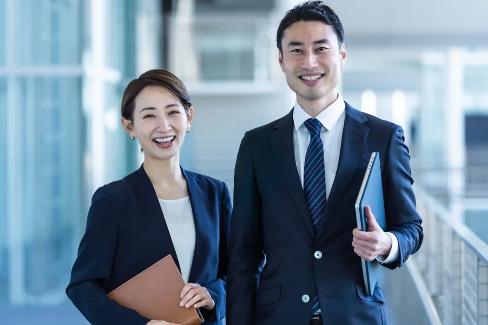 書類と端末を持ち笑顔で並ぶ男女の社員