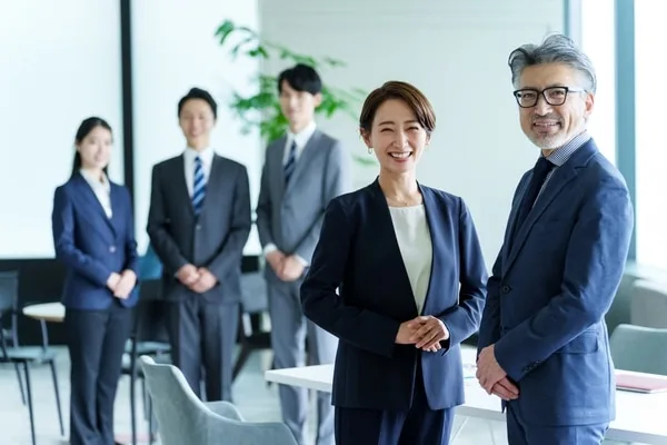 オフィスで並ぶ男女と背後に立つ社員3人