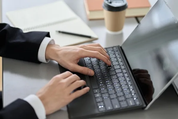 ビジネススーツを着た人がキーボードを操作しているデスク風景