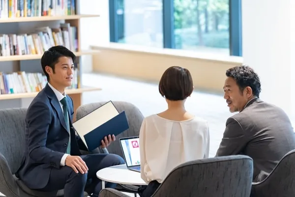 ビジネスパーソン3人が書類とノートパソコンで会議中