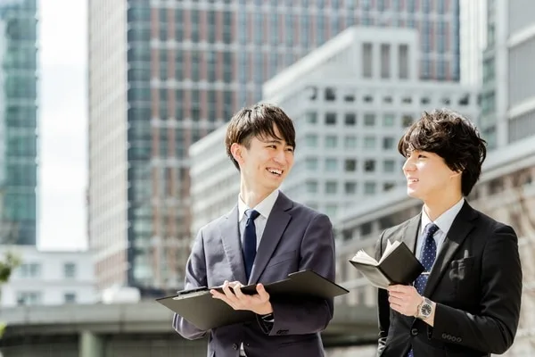 ビジネス街を背景に営業資料を持つ2人の男性営業担当者