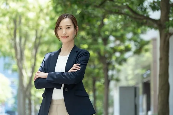 紺のテーラードジャケットを着た女性が腕を組んで笑顔で立つ