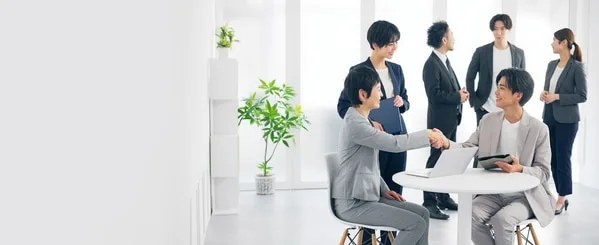 複数人がビジネスカジュアルで白いテーブルで握手し商談中