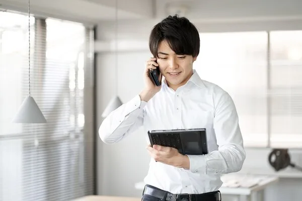 白いシャツの男性がタブレットを持ちながら電話で顧客対応中