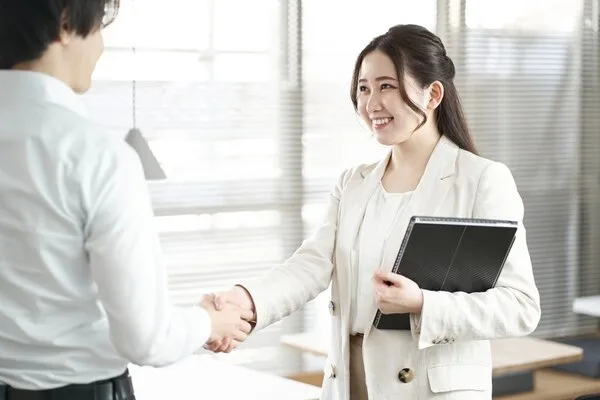 黒い手帳を持ち男性と握手する女性