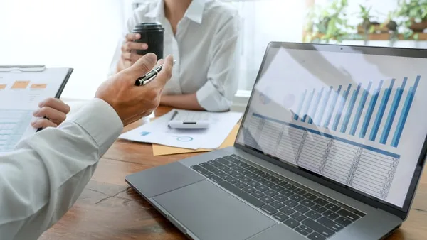 ノートパソコンにグラフを表示し営業データを打ち合わせする二人