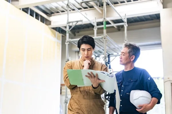 建設現場で作業員が書類を確認しながら打ち合わせしている様子
