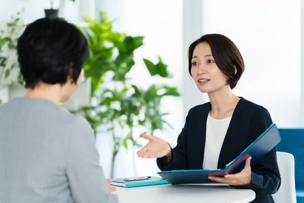 青いファイルを開いて相手に説明する女性社員