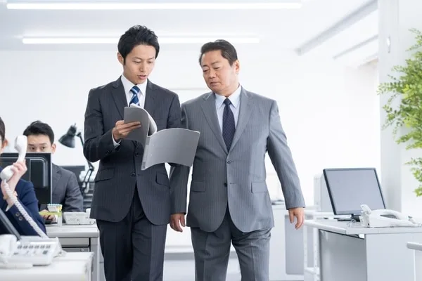 書類を手にオフィスを歩く男性社員2人