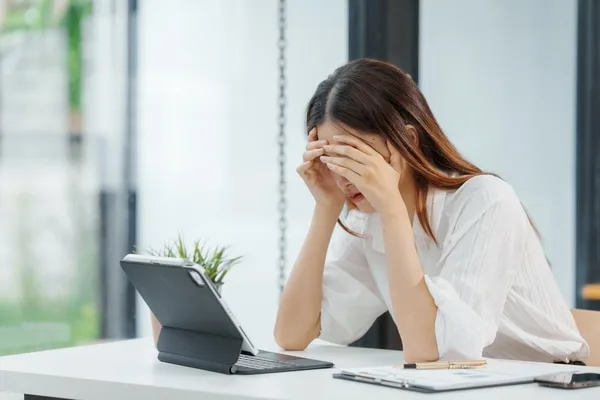 頭を抱えて困惑する女性とタブレット