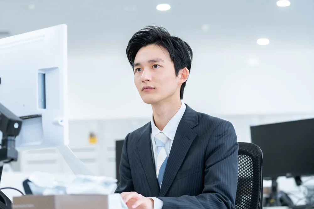 オフィスの机でパソコンを前に考える営業男性