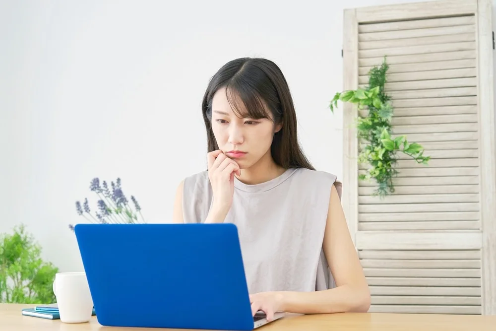 ノートパソコンを見つめながら考え込む女性