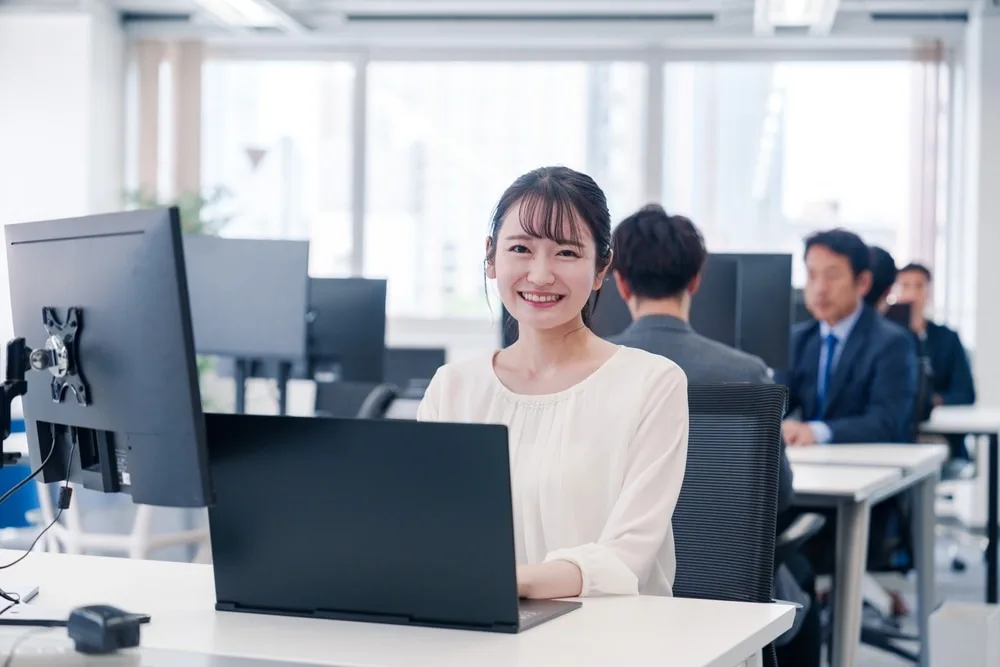 明るいオフィスでパソコンに向かい笑顔で仕事をする女性社員