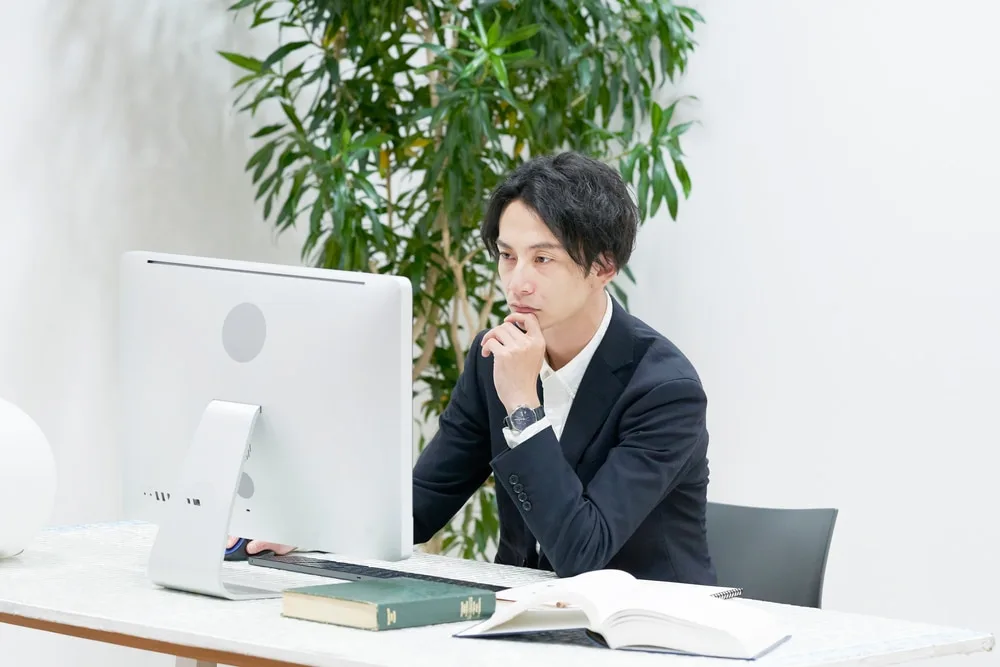デスクトップパソコンを前に、思案する表情でビジネスマン。