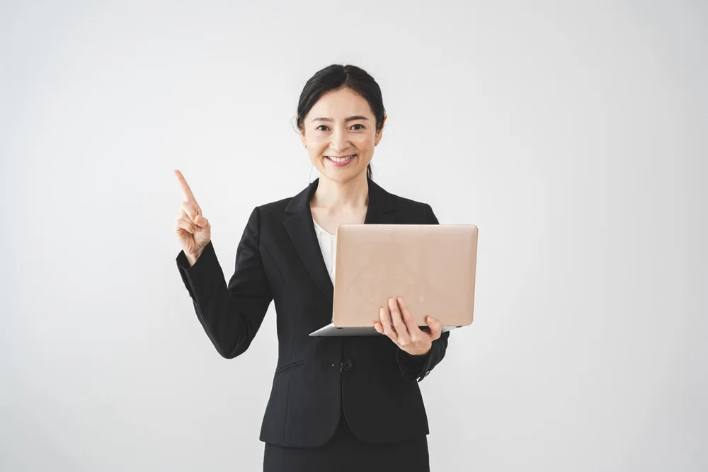 ノートパソコンを持ち人差し指を立てる女性