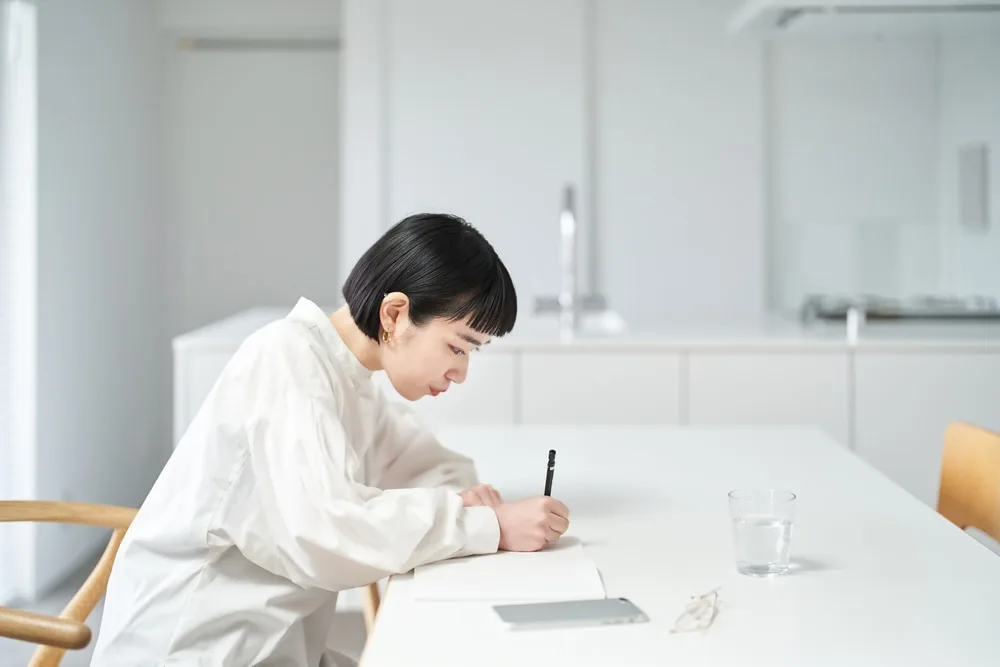 白いシャツを着た女性がテーブルで手紙を書いている