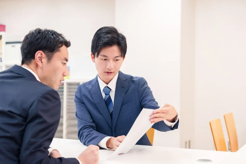営業担当者が顧客に書類を示しながら説明している会議シーン