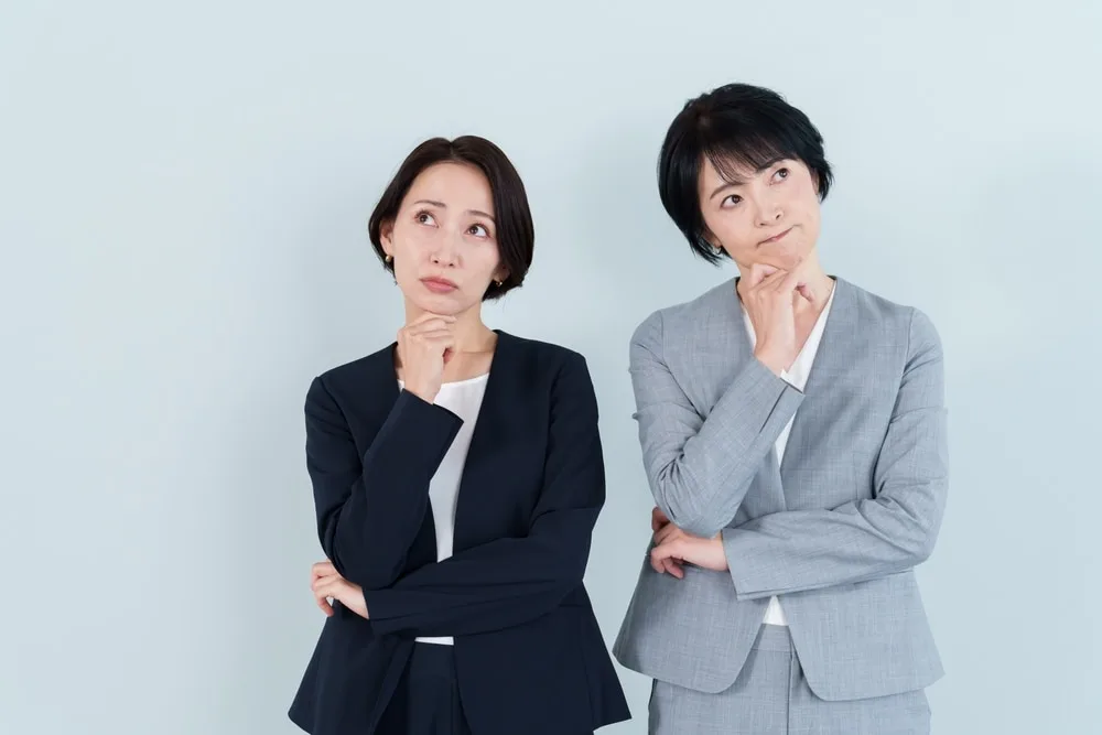 考える表情で上を見つめるビジネスウーマン二人。